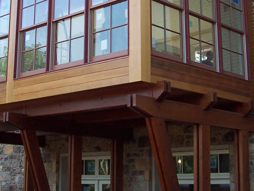 Redwood beams support a windowed room that bumps out from the main structure.